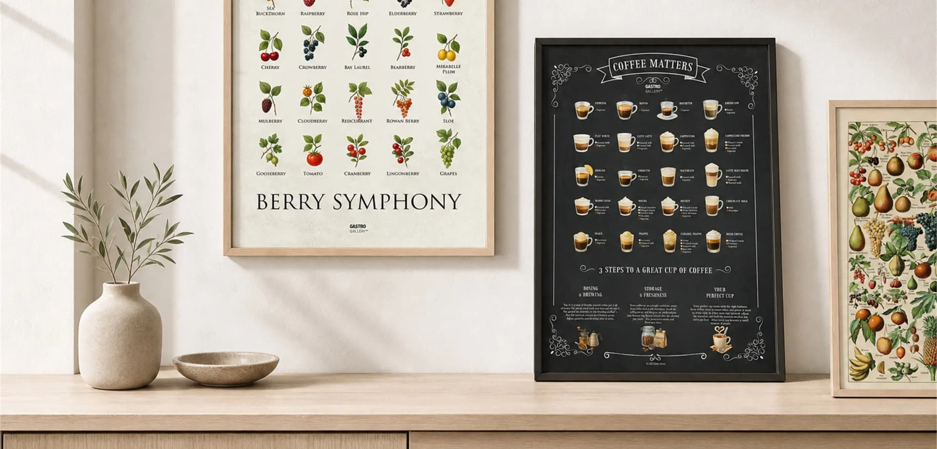A framed Berry Symphony print on the wall beside oak and black framed prints leaning on a sideboard