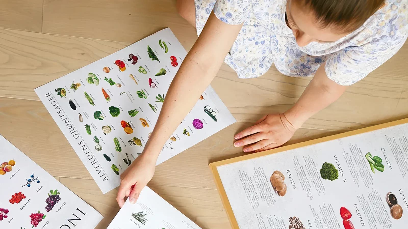 Overhead view of hands arranging illustrated food posters on a wooden floor